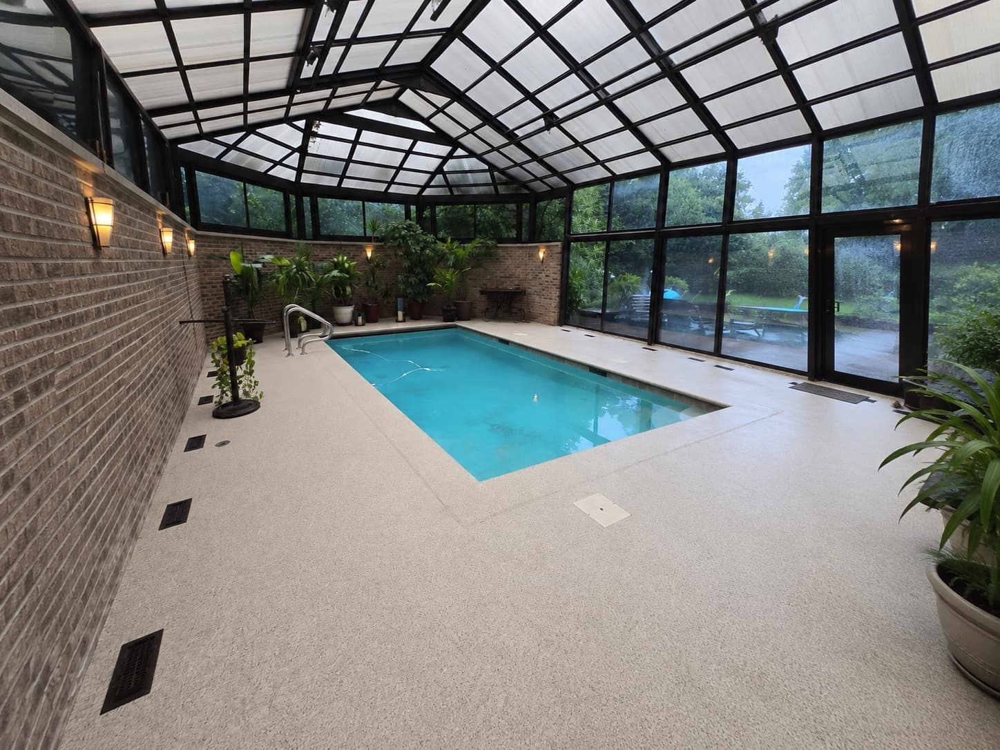 Indoor pool surrounded by a cream flake coated deck beneath a glass conservatory roof