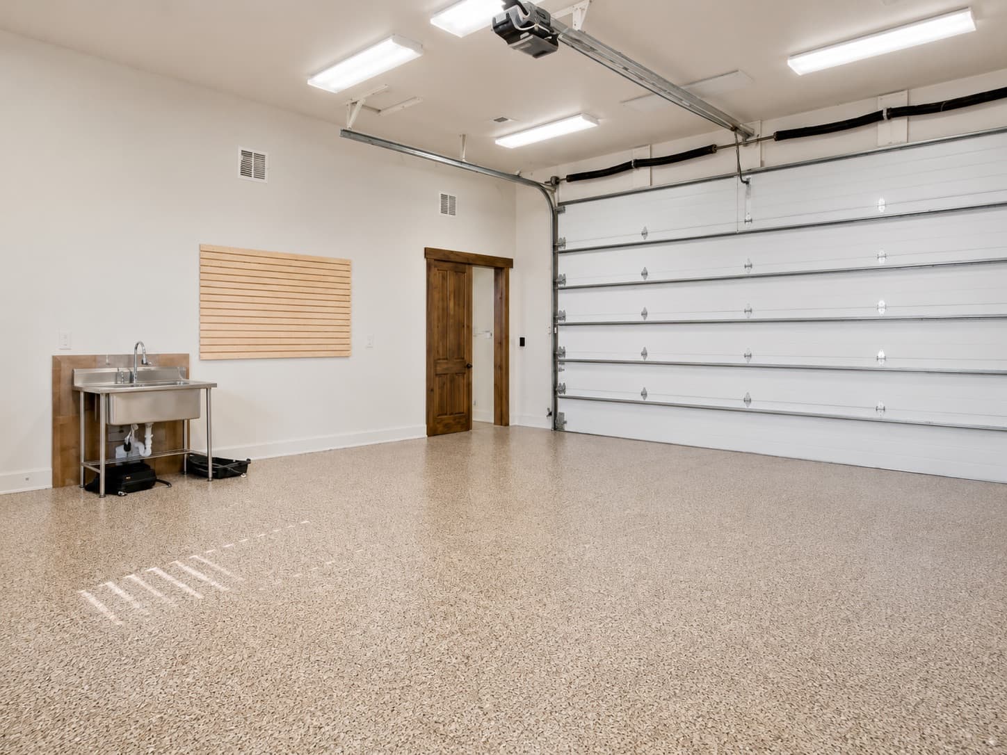 Tan full-flake polyurea garage floor coating by Revived Concrete Coatings in a bright two-car garage